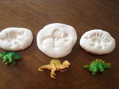 four plastic dinosaurs sitting next to each other on top of a wooden table in front of some cookies