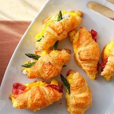 several croissants on a white plate with green leaves and bacon in them