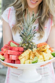 a woman holding a platter of fruit with pineapple and watermelon