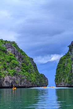 two kayakers are paddling through the water near some cliffs and green trees