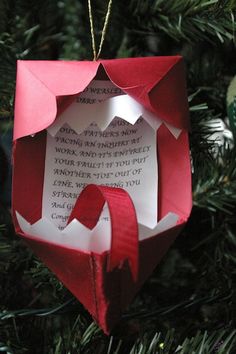 an ornament hanging from a christmas tree decorated with red paper and white writing