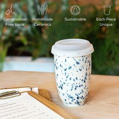 a coffee cup sitting on top of a wooden table next to a pen and paper