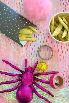 a table topped with pink and yellow items next to a bowl filled with pom poms