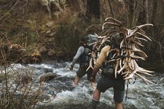 two people with backpacks walking across a river filled with water and deer antlers