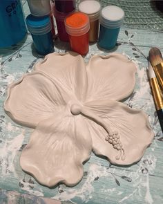 a white flower shaped object sitting on top of a table next to paint and brushes