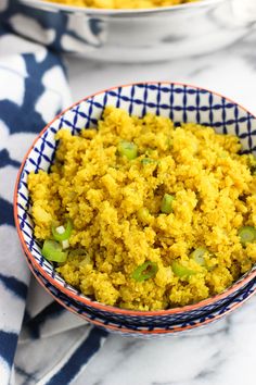 a bowl filled with yellow rice on top of a white and blue table cloth next to another bowl full of food