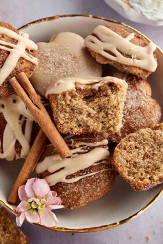 a bowl filled with cinnamon rolls covered in icing next to some cinnamon sticks and flowers