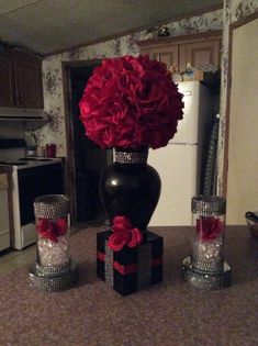 a vase filled with red flowers sitting on top of a counter next to two candles