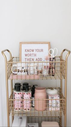 a gold metal shelf with pink and white items on it next to a framed sign that says know your worth then add