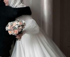 a bride and groom embracing each other in front of a white wall with flowers on it