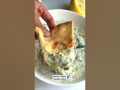 a person dipping some food into a bowl with crackers on it and lemons in the background