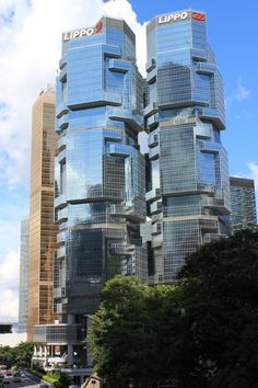 two very tall buildings next to each other on a street with trees in the foreground