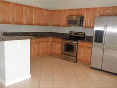 an empty kitchen with stainless steel appliances and wood cabinetry is pictured in this image