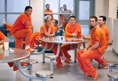 a group of men sitting around a table with chess pieces on it in orange outfits