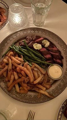 a plate with french fries, steak and green beans on it sitting on a table