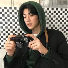 a person taking a photo with a camera in front of a tiled wall and black and white tiles