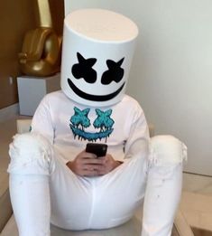 a person sitting on a chair with a cell phone in their hand and wearing a marshmallow hat