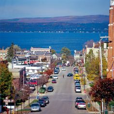 a city street with cars parked on both sides and the ocean in the back ground