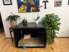 a dog cage with plants on the floor next to it and a painting hanging above