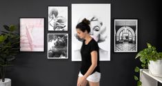 a woman walking in front of a wall with pictures on it and potted plants