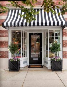 a black and white striped awning over a store front door with potted plants