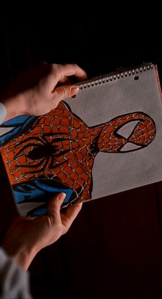 a person holding a notebook with a drawing of a spider - man on the cover