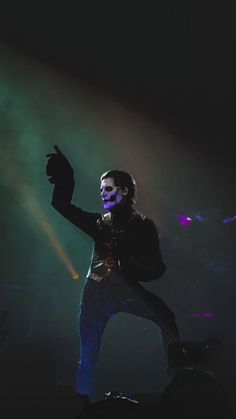 the man is performing on stage with his hands in the air and lights behind him