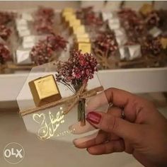 a person holding a small vase with flowers in it and some chocolates on the table