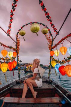 a woman is sitting on the bow of a boat with lanterns floating in the water