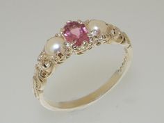 This charming vintage style ring is set with a central 6x4mm natural pink tourmaline with a 4mm freshwater pearl either side. It has a beautiful carved scroll design on the shoulders, which offsets the polished white gold. The ring can be made in 9,10, 14 or 18K gold.  Please note that due to the individual nature of natural gemstones the colour of stones may vary between rings. If you have specific requirements for the stone, please contact our friendly team and we'll do our best to accommodate Trilogy Ring, Magical Jewelry, Jewelry Lookbook, Pretty Rings, Girly Jewelry, Jewelry Inspo, Dream Jewelry, Stylish Jewelry