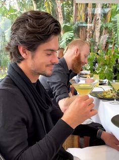 two men sitting at a table with wine glasses in their hands and food on the table