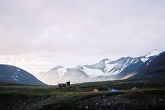 the mountains are covered in snow and grass, with tents set up on the ground