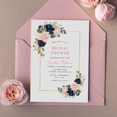 a pink and blue floral bridal shower card on top of a pink envelope next to flowers