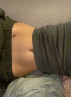 a woman laying on top of a bed next to a wall with a tattoo on her stomach