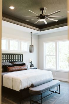 a bedroom with a bed, ottoman and ceiling fan in it's center area