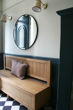 a wooden bench sitting in front of a round mirror on the wall next to a black and white checkered floor