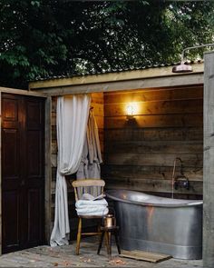 an outdoor bathroom with a large tub and wooden walls, next to a door that has curtains on it