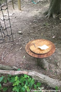 a wooden table sitting on top of a forest floor next to a tree trunk and fence