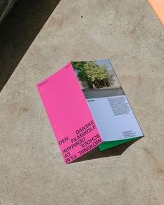 a pink and green book sitting on top of a cement floor next to a bench