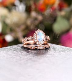 a white opal and diamond ring sitting on top of a table with flowers in the background