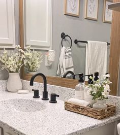 a bathroom sink sitting under a mirror next to a white towel rack and vase with flowers