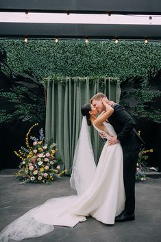 a bride and groom kissing in front of a green backdrop