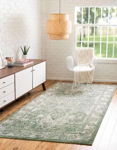 a living room with white furniture and a green rug on the wooden floor next to a window