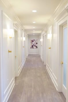 a long hallway with white walls and wood floors is lit by recessed light fixtures