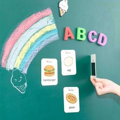 a person holding a cell phone in front of a chalkboard with letters and pictures on it