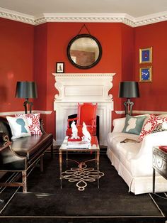 a living room with red walls and black carpeted flooring, white couches and chairs