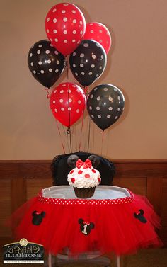 a table topped with balloons and a cupcake on top of a red tutu