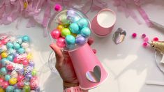 a person is holding a pink cup filled with colorful easter eggs and other decorations on a table