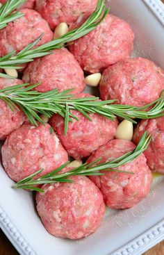 raw meatballs with rosemary sprigs in a white dish on a wooden table