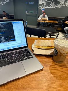 a laptop computer sitting on top of a wooden table next to a cup of coffee